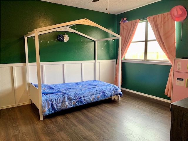 bedroom with a textured ceiling, wood finished floors, wainscoting, and a decorative wall