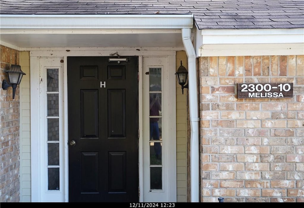 property entrance featuring brick siding and roof with shingles