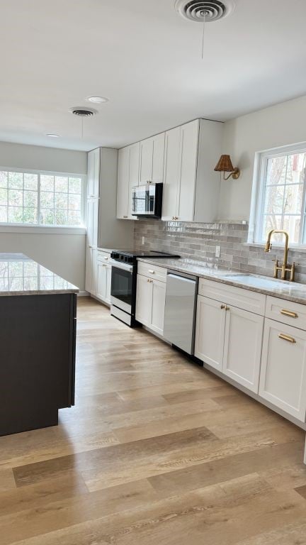 kitchen featuring visible vents, a sink, tasteful backsplash, stainless steel appliances, and light wood-style floors