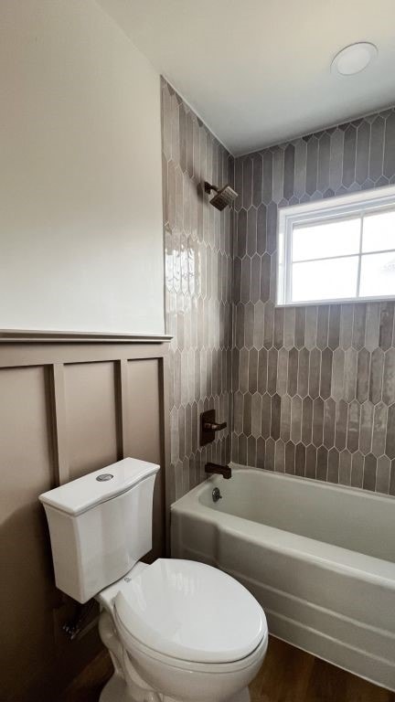 bathroom with a wainscoted wall, toilet, wood finished floors, shower / washtub combination, and a decorative wall