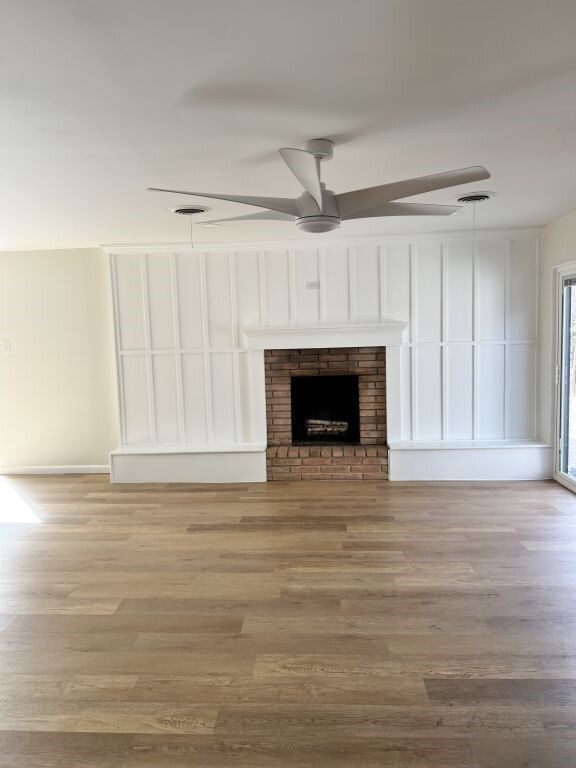 unfurnished living room featuring a fireplace, wood finished floors, visible vents, and ceiling fan