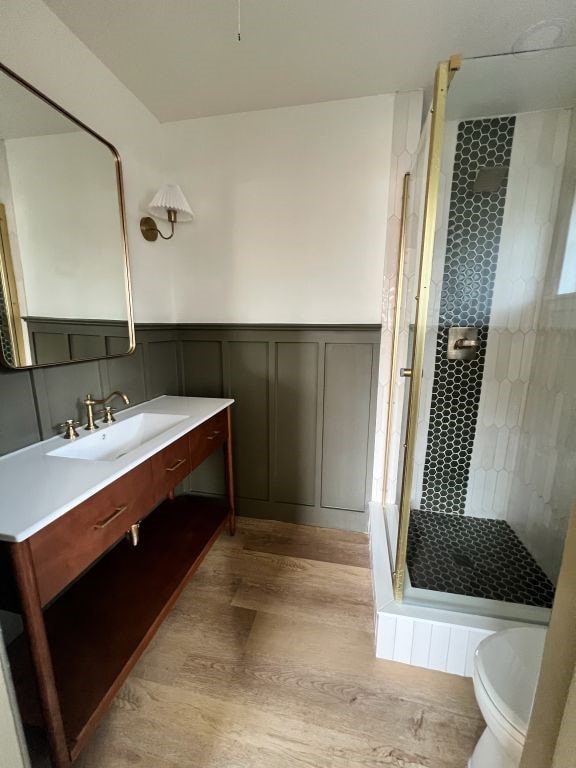 full bath with toilet, wainscoting, a stall shower, wood finished floors, and vanity