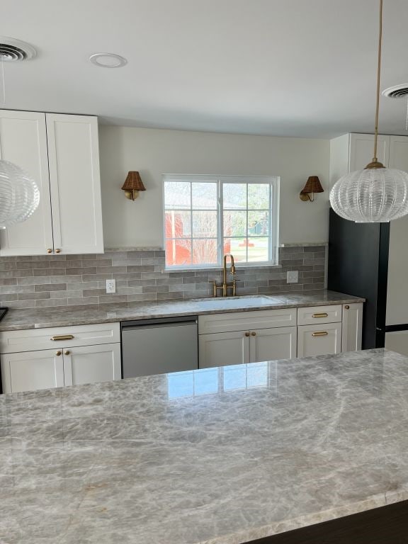 kitchen featuring backsplash, light stone counters, stainless steel dishwasher, white cabinets, and a sink