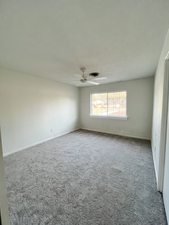 carpeted spare room featuring baseboards, visible vents, and ceiling fan