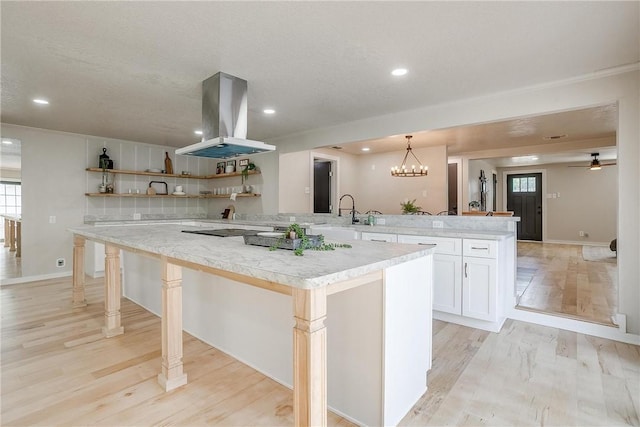 kitchen featuring a breakfast bar, hanging light fixtures, white cabinetry, island range hood, and kitchen peninsula