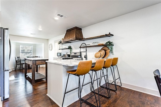 kitchen featuring kitchen peninsula, appliances with stainless steel finishes, a kitchen breakfast bar, premium range hood, and dark hardwood / wood-style floors