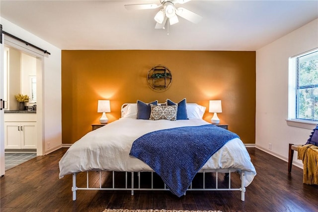 bedroom with dark hardwood / wood-style floors, ceiling fan, a barn door, and ensuite bath