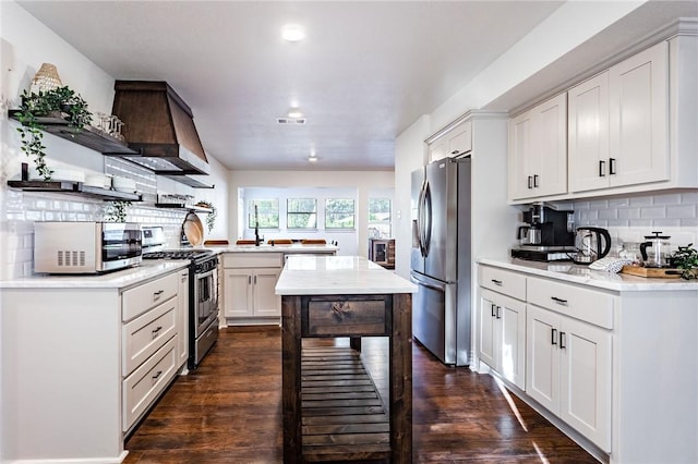 kitchen with white cabinets, wall chimney range hood, decorative backsplash, appliances with stainless steel finishes, and dark hardwood / wood-style flooring