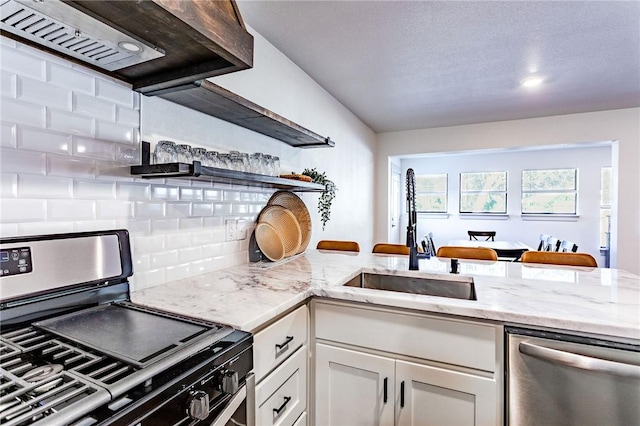 kitchen with sink, tasteful backsplash, light stone counters, white cabinets, and appliances with stainless steel finishes