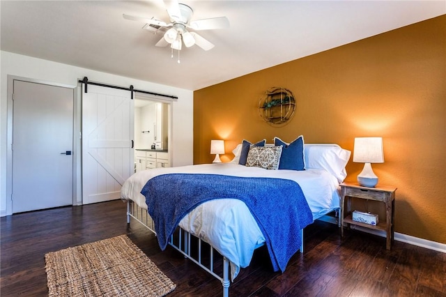 bedroom featuring a barn door, ceiling fan, ensuite bath, and dark hardwood / wood-style floors