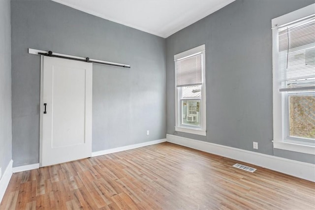 spare room with a healthy amount of sunlight, light wood-type flooring, and a barn door