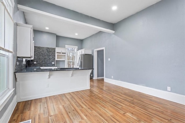 kitchen with white cabinetry, stainless steel refrigerator, decorative backsplash, sink, and kitchen peninsula