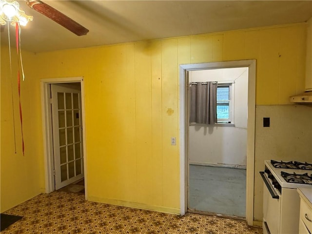 interior space featuring extractor fan, white range with gas cooktop, ceiling fan, and wood walls