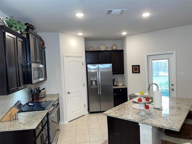 kitchen featuring light stone counters, light tile patterned floors, a kitchen island with sink, and appliances with stainless steel finishes