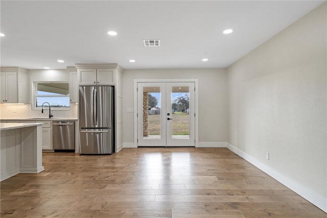 kitchen featuring french doors, light wood-type flooring, tasteful backsplash, stainless steel appliances, and white cabinetry