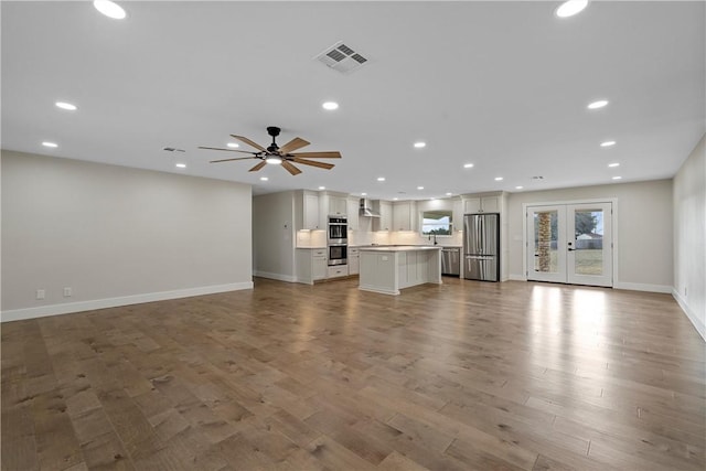 unfurnished living room with ceiling fan, french doors, and light hardwood / wood-style floors