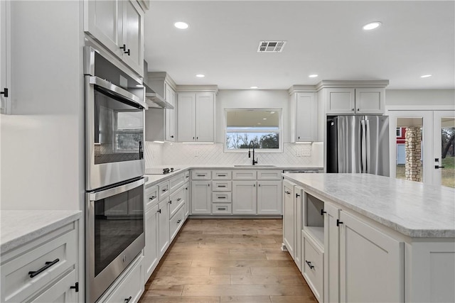 kitchen featuring backsplash, stainless steel appliances, sink, light hardwood / wood-style flooring, and white cabinets