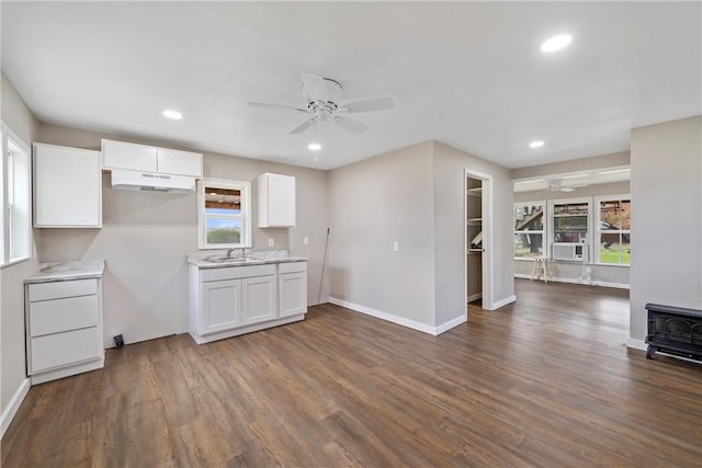 kitchen with dark hardwood / wood-style flooring, ceiling fan, sink, white cabinetry, and a wood stove