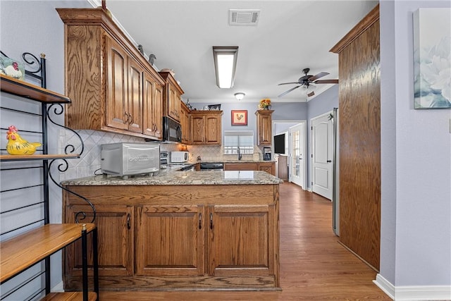 kitchen featuring sink, kitchen peninsula, ceiling fan, light hardwood / wood-style floors, and decorative backsplash