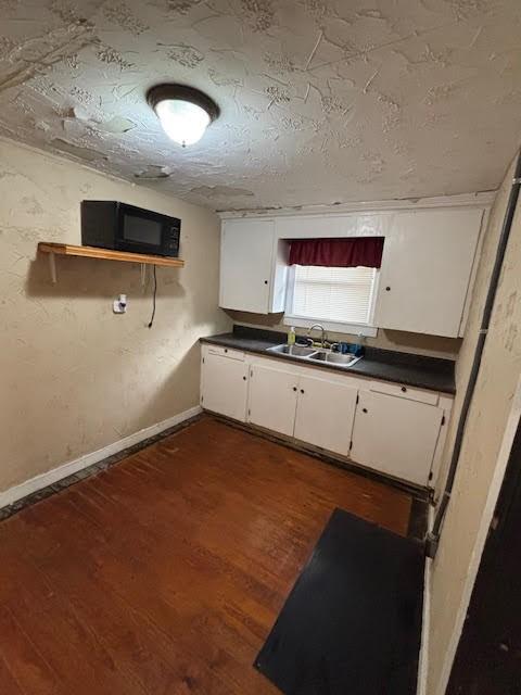 kitchen with a sink, dark countertops, white cabinets, black microwave, and dark wood-style flooring