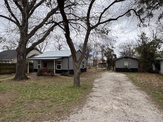 view of front of property featuring metal roof, a porch, driveway, and fence