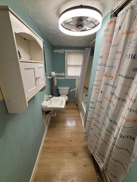 bathroom featuring wood finished floors, baseboards, a sink, curtained shower, and toilet