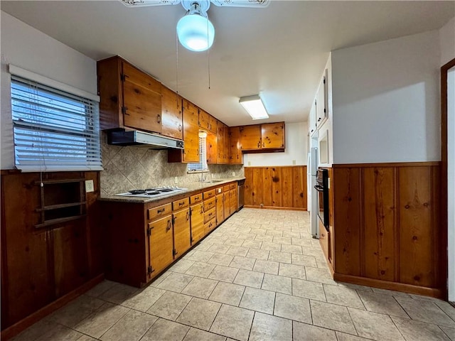 kitchen featuring wood walls, white gas stovetop, backsplash, oven, and sink