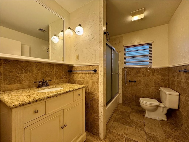 full bathroom featuring combined bath / shower with glass door, vanity, toilet, and tile walls