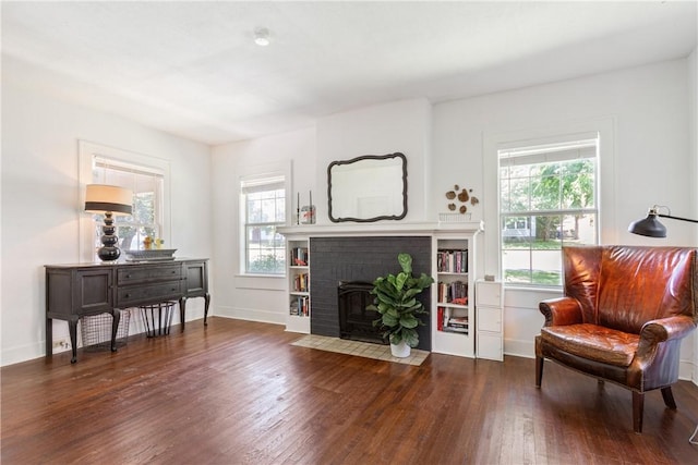 sitting room with a brick fireplace and dark wood-type flooring