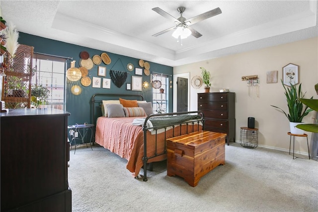 carpeted bedroom featuring multiple windows, a raised ceiling, and ceiling fan