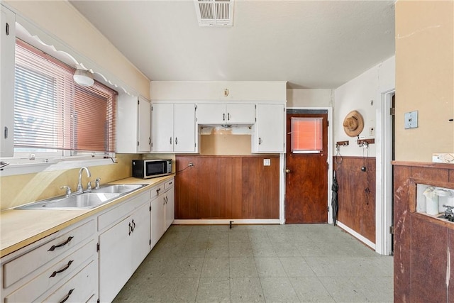 kitchen with a wainscoted wall, light countertops, stainless steel microwave, white cabinetry, and a sink