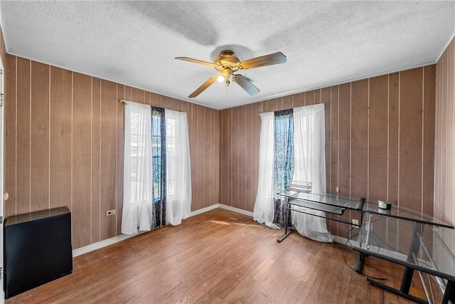 spare room with a textured ceiling, wood finished floors, a ceiling fan, and a healthy amount of sunlight