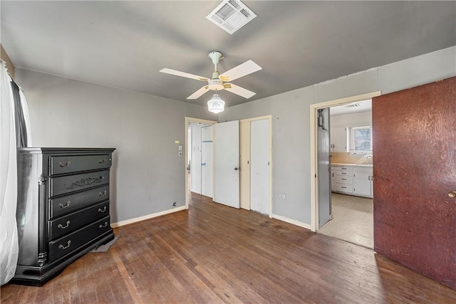 unfurnished bedroom featuring a ceiling fan, visible vents, baseboards, and wood finished floors