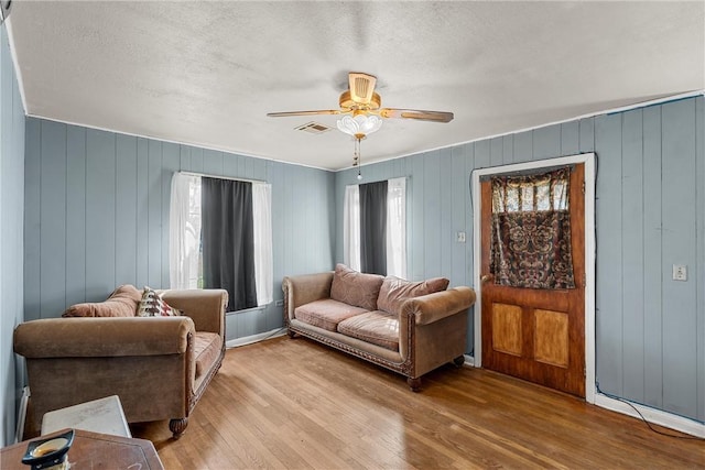 living area featuring a ceiling fan, visible vents, light wood-style flooring, and a textured ceiling