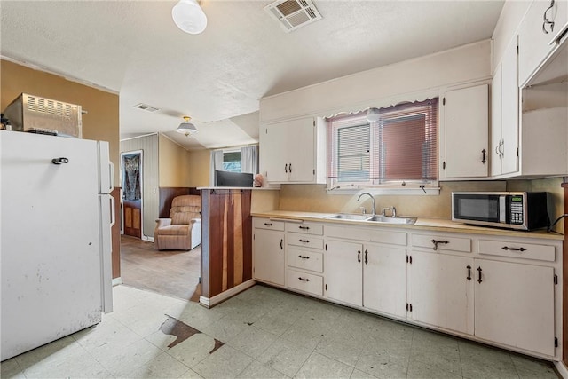 kitchen with visible vents, stainless steel microwave, freestanding refrigerator, light floors, and a sink