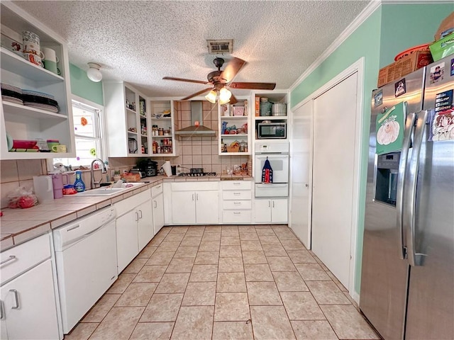 kitchen with white cabinets, wall chimney range hood, sink, tile counters, and stainless steel appliances