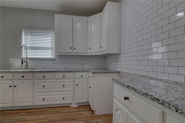 kitchen with sink, decorative backsplash, light hardwood / wood-style floors, light stone counters, and white cabinetry