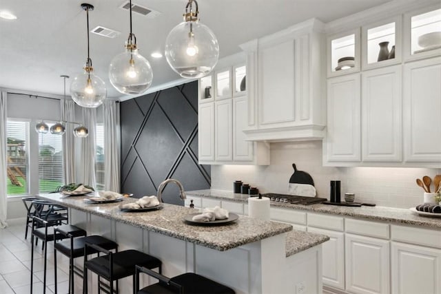 kitchen with white cabinets, stainless steel gas cooktop, and a kitchen island with sink