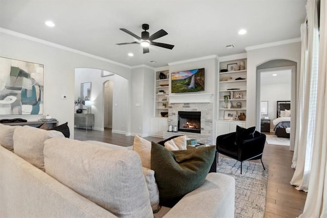 living room featuring hardwood / wood-style flooring, a stone fireplace, ceiling fan, and crown molding