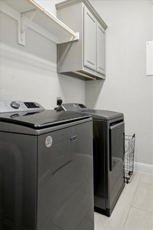 laundry area featuring separate washer and dryer, light tile patterned floors, and cabinets