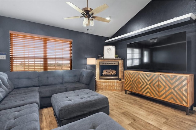 living area with lofted ceiling, a fireplace with raised hearth, ceiling fan, and wood finished floors