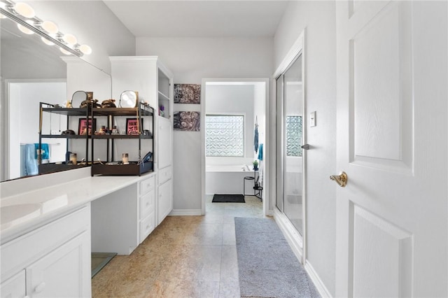 full bath featuring a stall shower, a garden tub, vanity, and baseboards