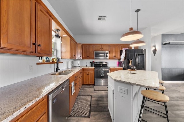 kitchen with appliances with stainless steel finishes, light stone counters, a breakfast bar, dark wood-type flooring, and sink