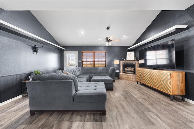 living room featuring ceiling fan, hardwood / wood-style floors, lofted ceiling, and a brick fireplace