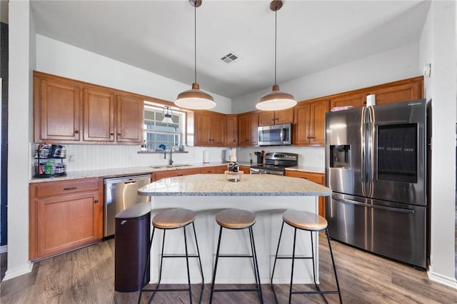 kitchen with a center island, stainless steel appliances, visible vents, hanging light fixtures, and a sink