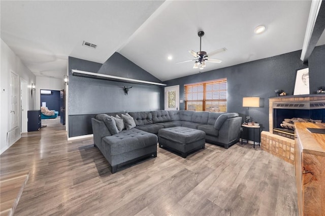 living area with lofted ceiling, a fireplace, wood finished floors, visible vents, and a ceiling fan