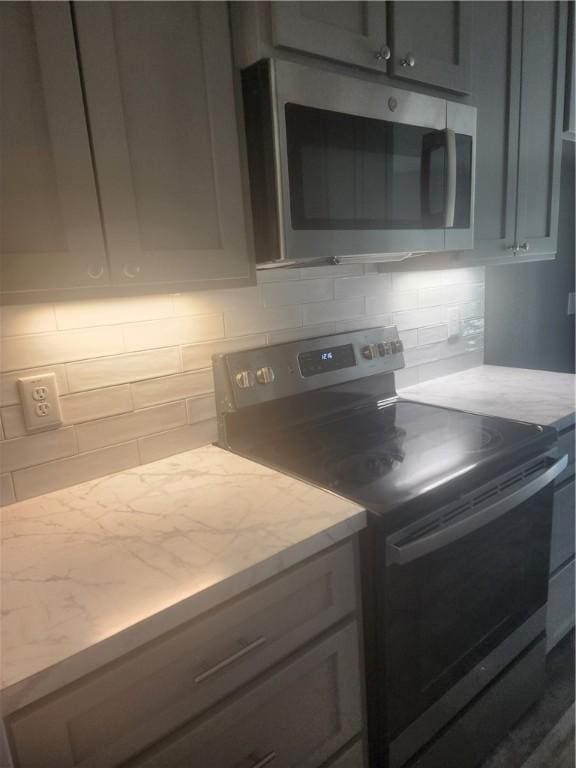 kitchen with backsplash, gray cabinetry, light stone countertops, and stainless steel appliances