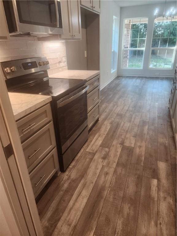 kitchen featuring light stone countertops, backsplash, stainless steel appliances, dark wood-type flooring, and decorative light fixtures