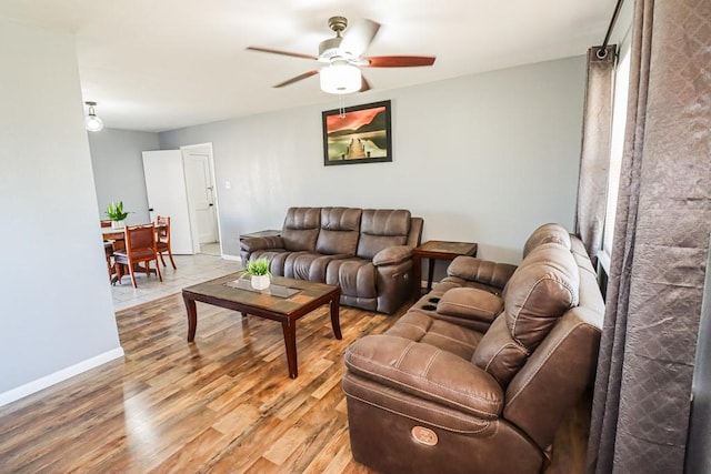 living area featuring ceiling fan, light wood-style flooring, and baseboards