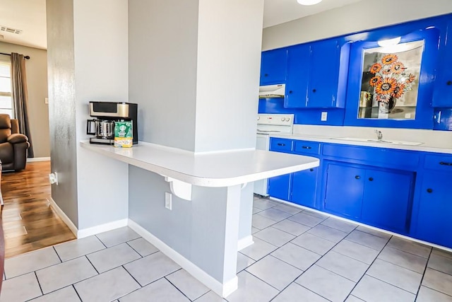 kitchen featuring blue cabinets, under cabinet range hood, light countertops, and a sink